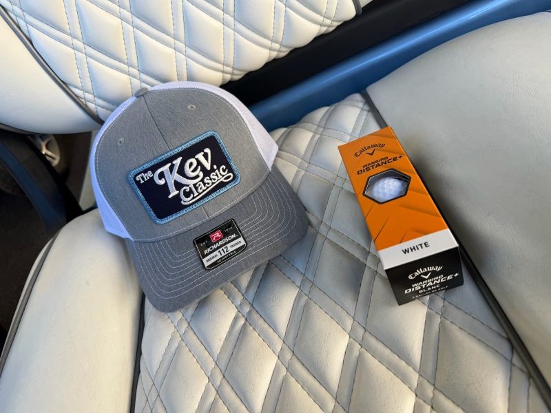 A Kev Classic hat and golf balls on a golf cart seat